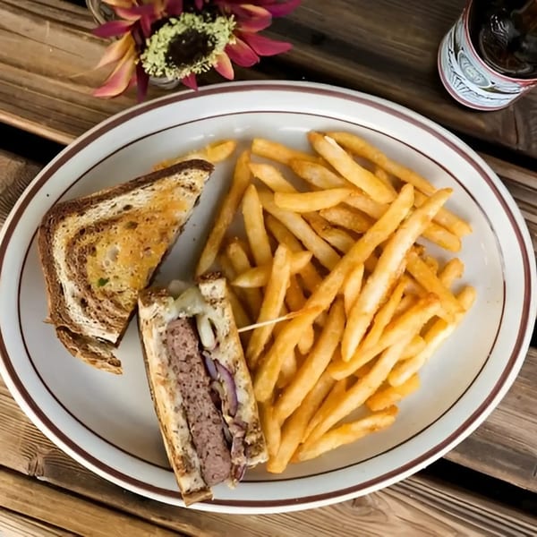 A Dixie's Home Cookin' patty melt with fries on a white plate, on a wooden table.