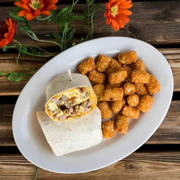 Breakfast burrito with eggs, sausage, and cheese, served with tater tots on a white plate.